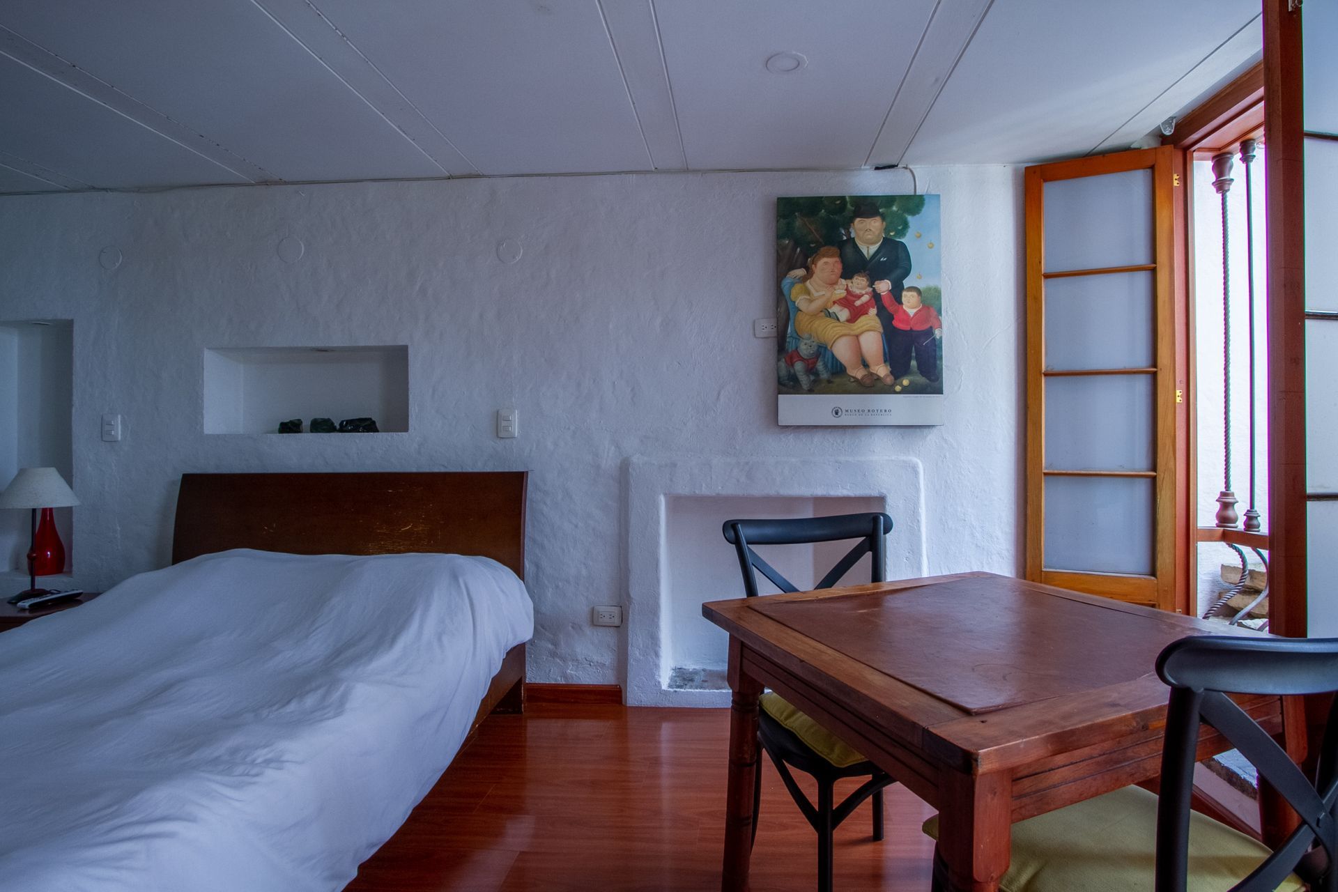 A bedroom with a bed , table , chairs and a painting on the wall.