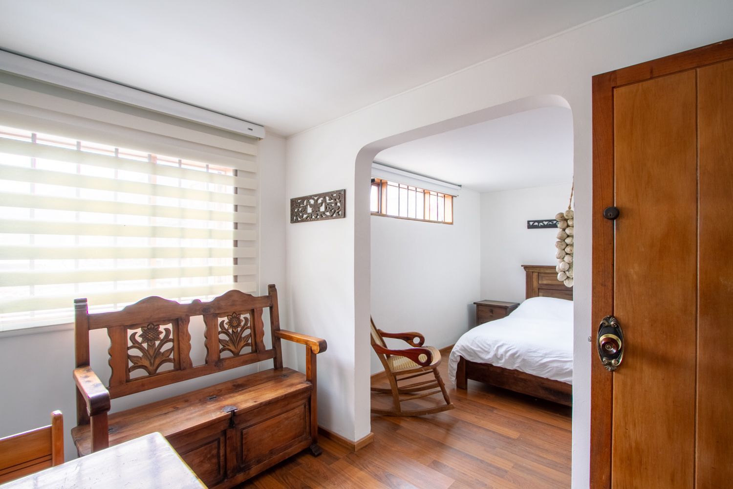 A bedroom with a wooden bench , rocking chair and bed.