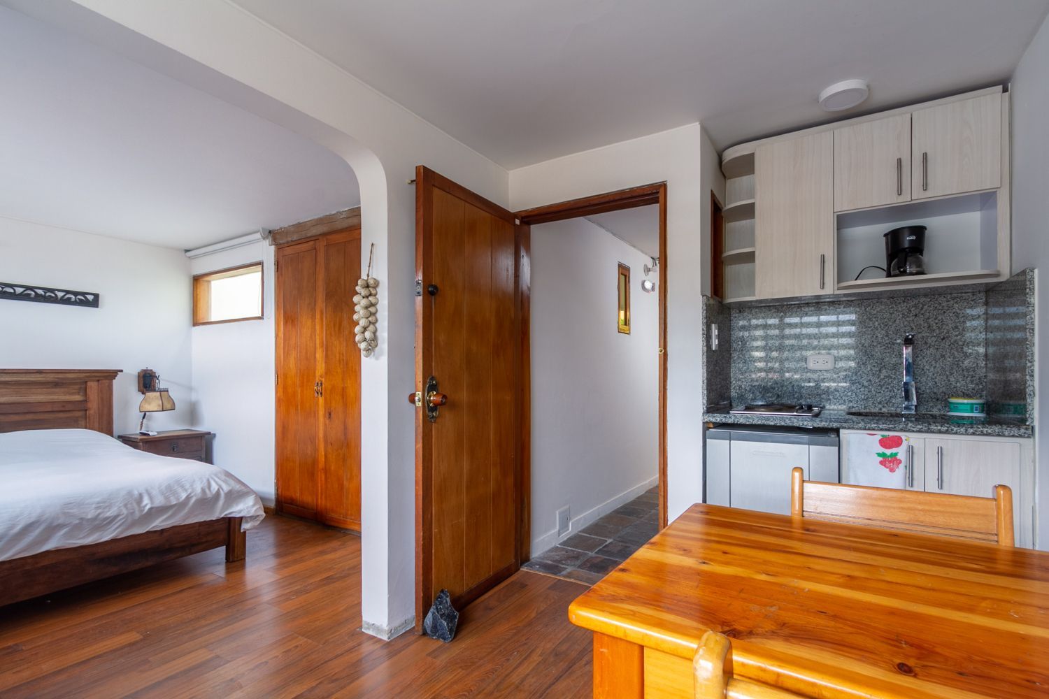 A bedroom with a bed , table , chairs and a kitchen.