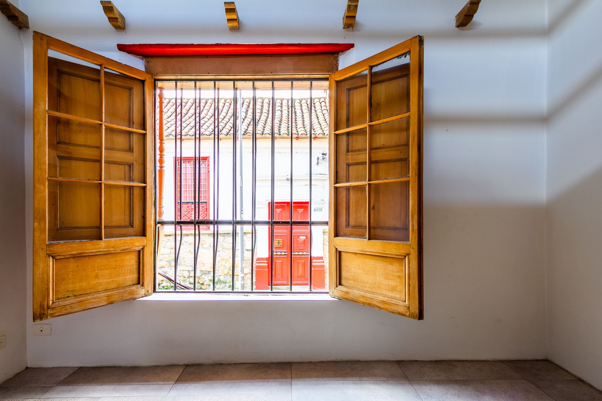An empty room with a window with shutters open and a red door.