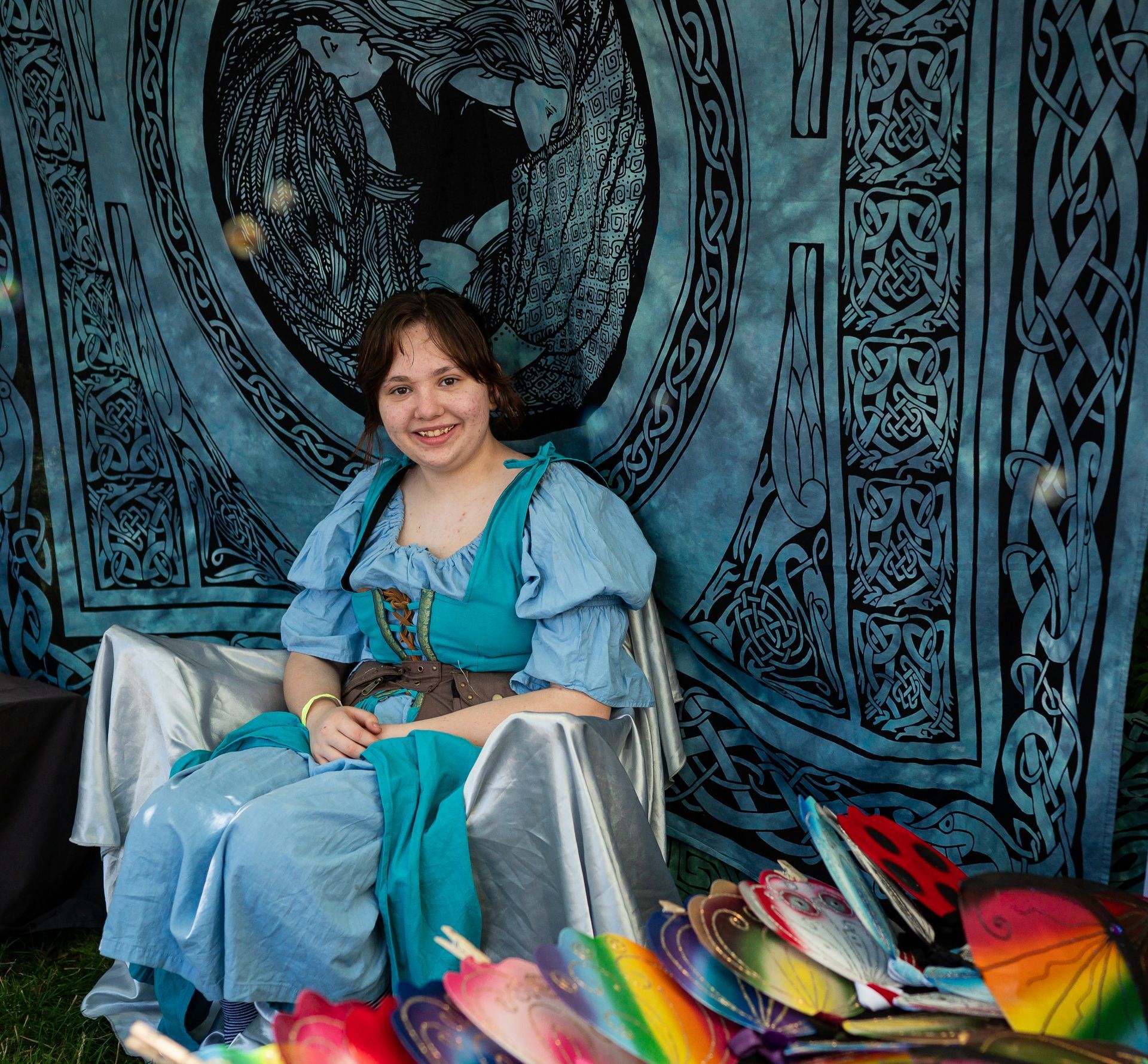 A woman in a blue dress is sitting in front of a blue tapestry