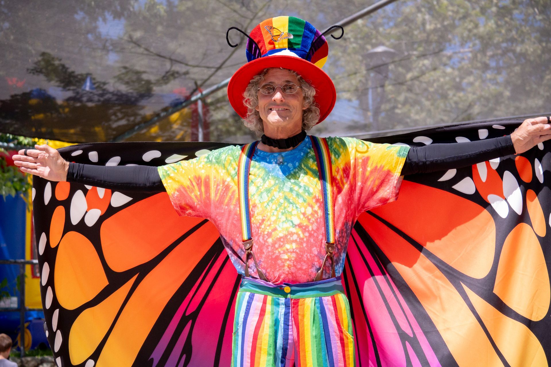 A woman in a clown costume with butterfly wings is standing with her arms outstretched.