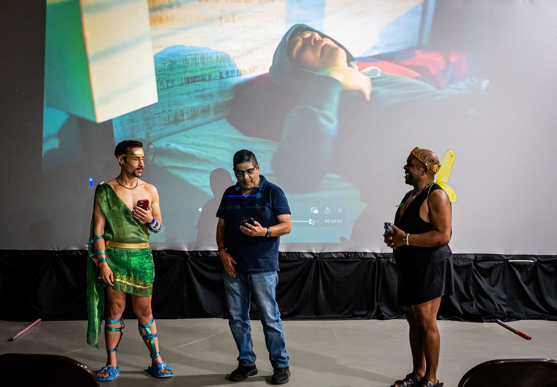 Three people are standing on a stage in front of a large screen.