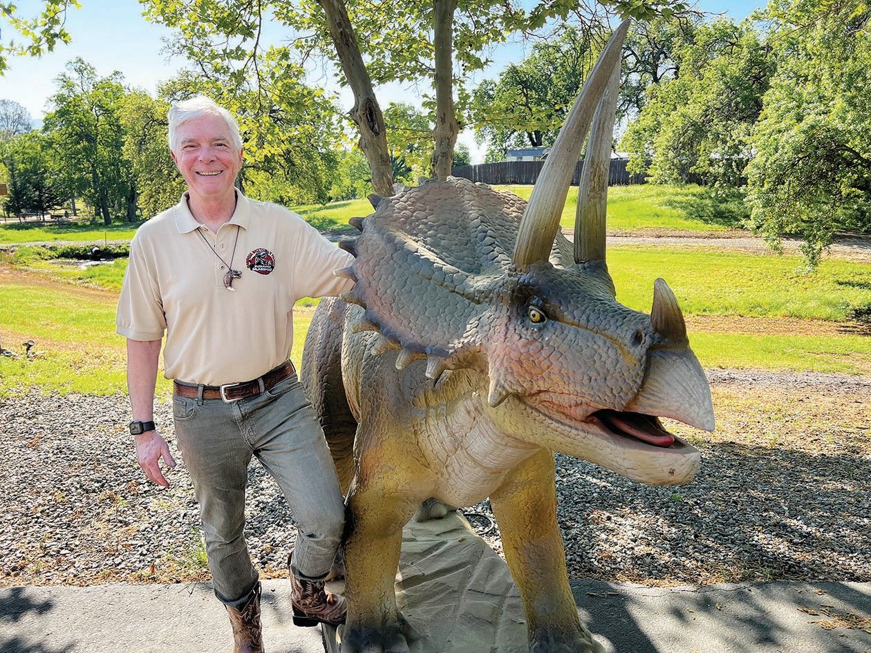 A man is standing next to a dinosaur statue in a park.