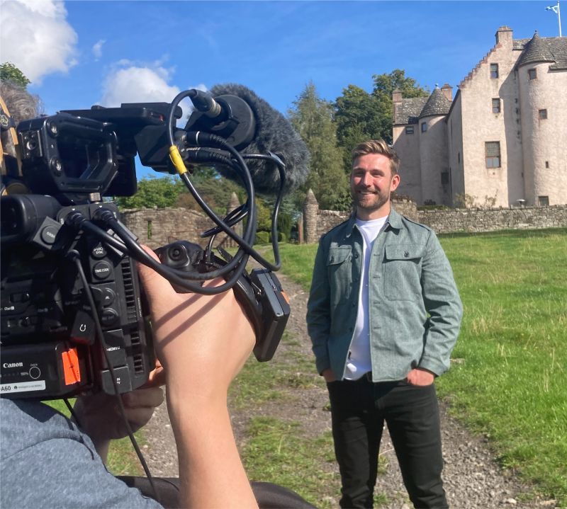 A man in a green jacket is being filmed by a camera