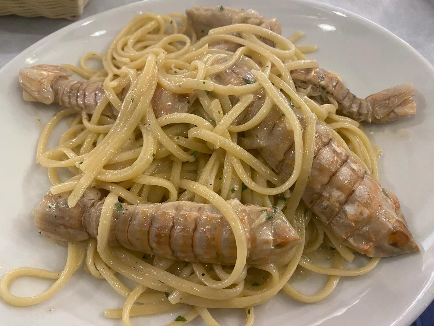 Un piatto bianco con sopra spaghetti e gamberi su un tavolo.