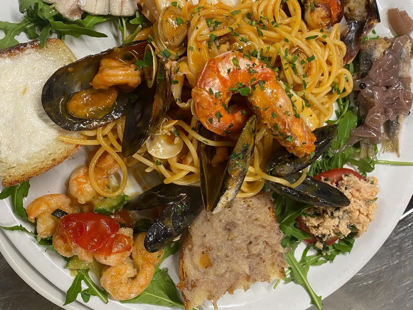 Un piatto di cibo con tagliatelle, gamberetti, cozze e pane su un tavolo.