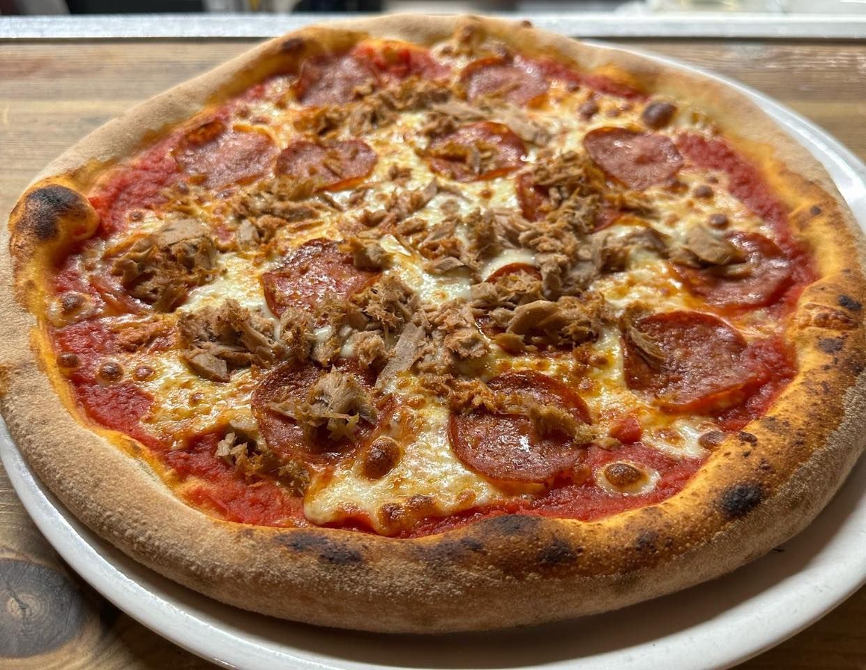 Una pizza con salame piccante e salsiccia su un piatto bianco su un tavolo.