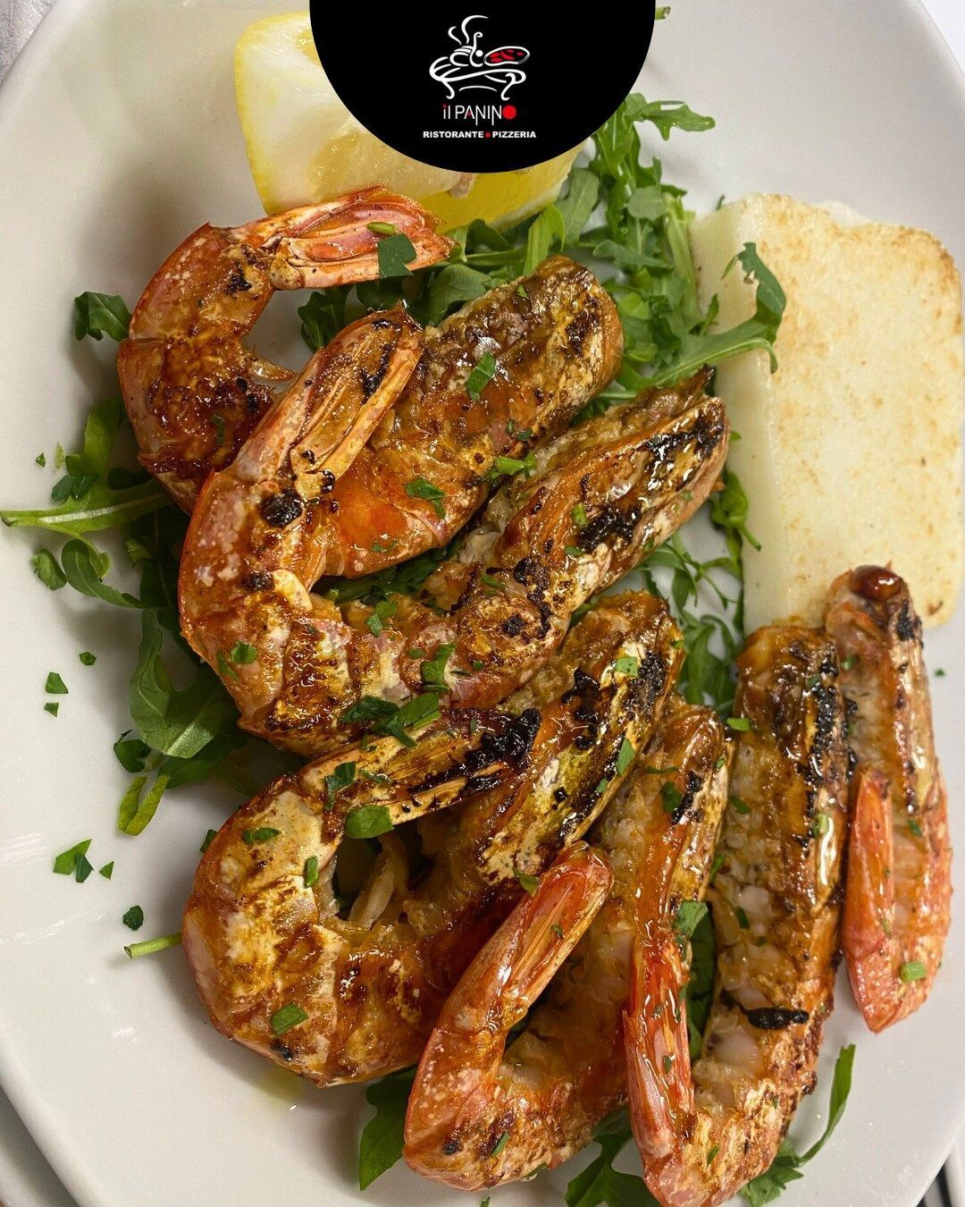 Un piatto bianco condito con gamberi grigliati e pane