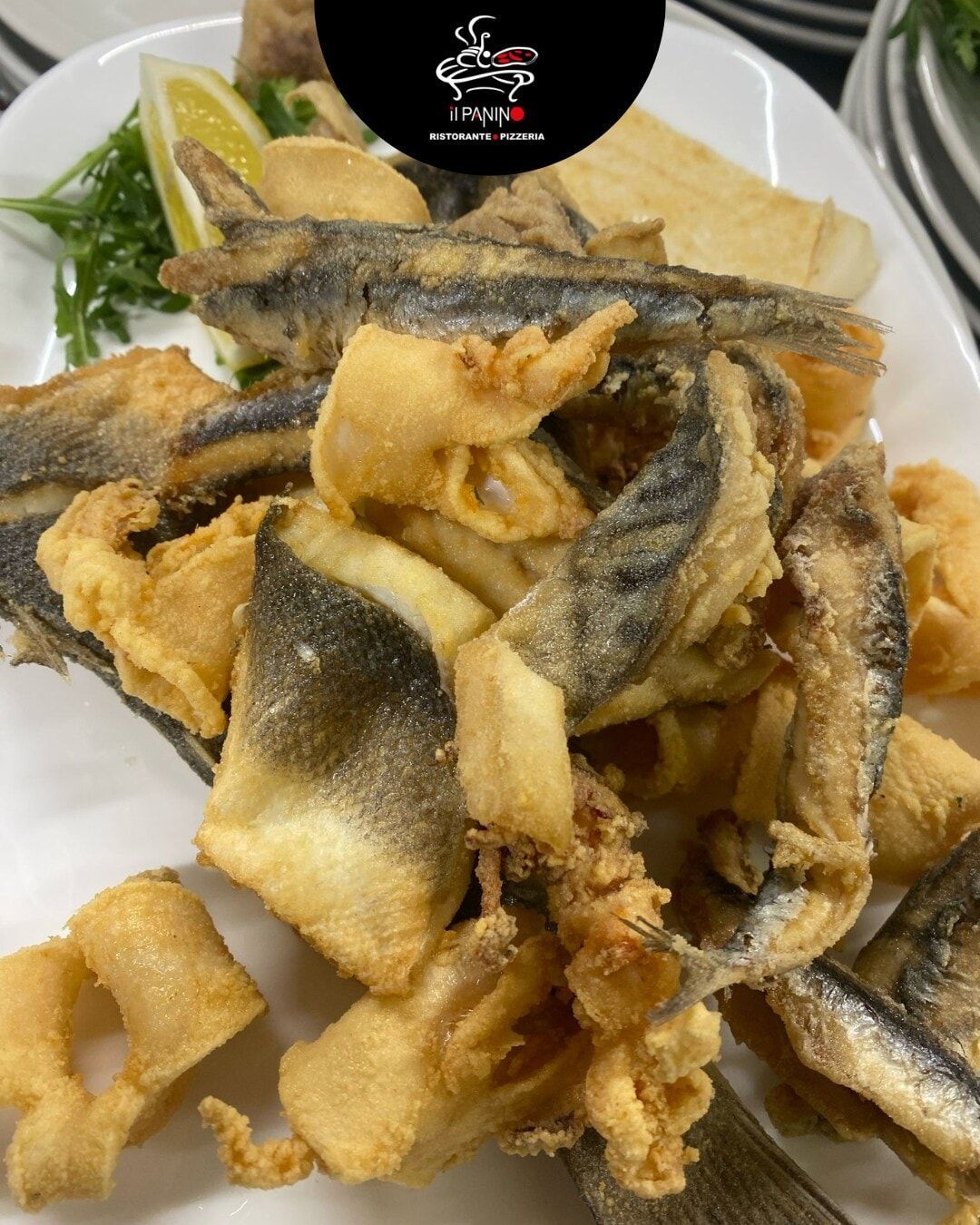 Un piatto bianco con sopra pesce fritto e patatine fritte
