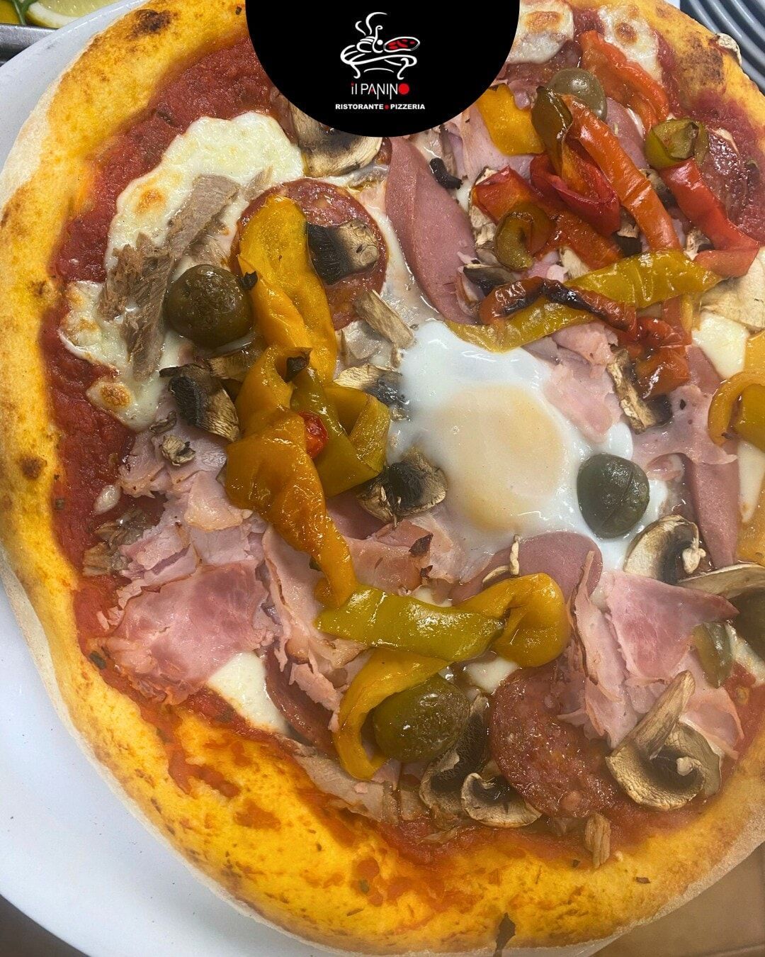 Una pizza con tanti condimenti è servita su un piatto bianco.