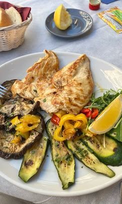 Un piatto bianco con pollo e verdure su un tavolo.