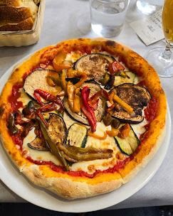 Una pizza con le verdure sopra è su un piatto bianco su un tavolo.