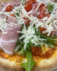 Una pizza con prosciutto, pomodori, formaggio e lattuga su un piatto.