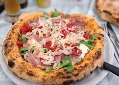 Una pizza con prosciutto, pomodori e formaggio su un piatto bianco.