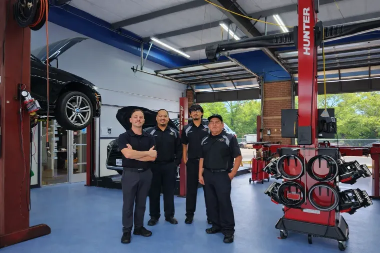 Three mechanics standing in an auto repair shop in alvin texas under lifts, with a car raised in the background.