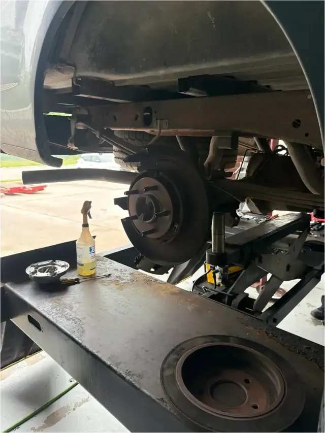 Mechanic removing a brake drum from a vehicle wheel, with hands over a bucket in a garage.