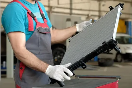 Worker in gloves holding a car radiator in an auto repair shop