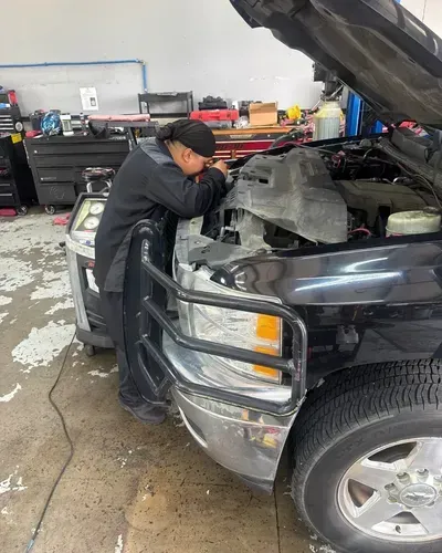 Mechanic inspecting engine of a black pickup truck in a garage, hood open.