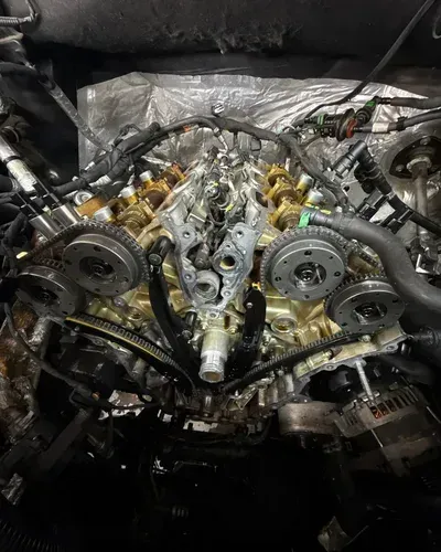 Close-up of an exposed car engine with belts, pulleys, and metallic components in a workshop.