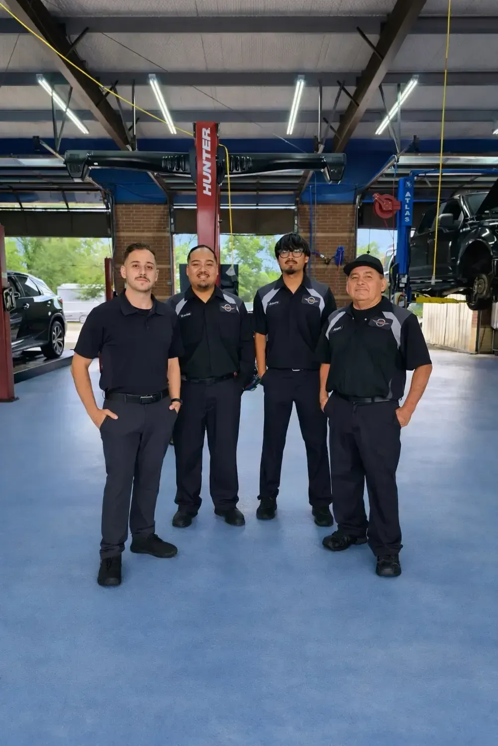 Four people in black uniforms standing together in a covered parking area with blue flooring.