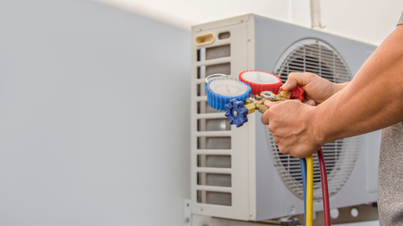 Hands connecting gauges to an air conditioner unit for servicing, outdoors.