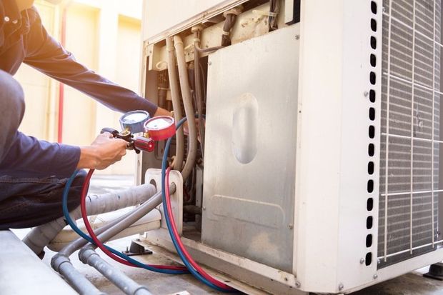 HVAC technician repairing an air conditioning unit outdoors; using gauges and hoses.