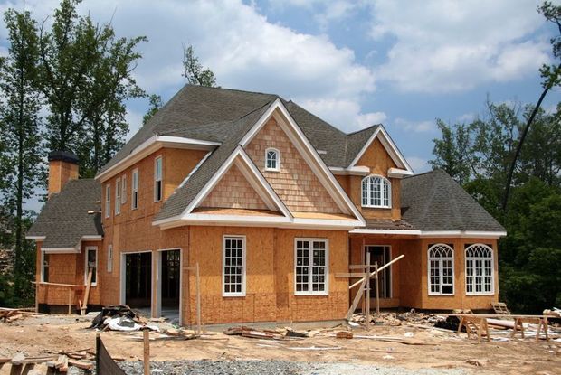 House under construction, wooden frame, unfinished exterior, windows installed, sunny day, outdoor setting.