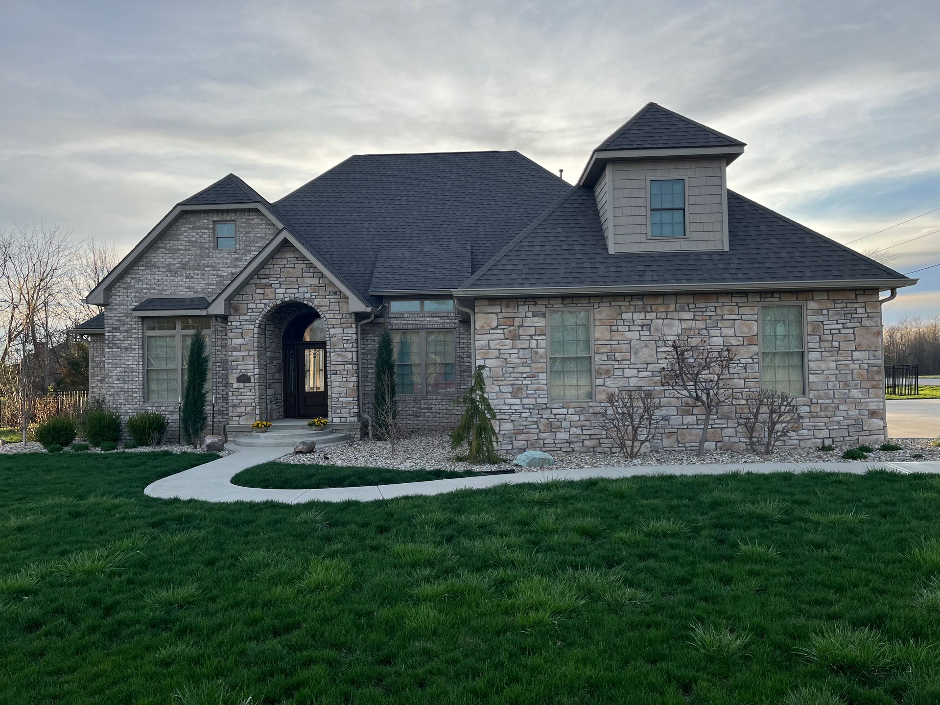 Roofer in safety vest using a nail gun on a shingled roof under a bright sky.