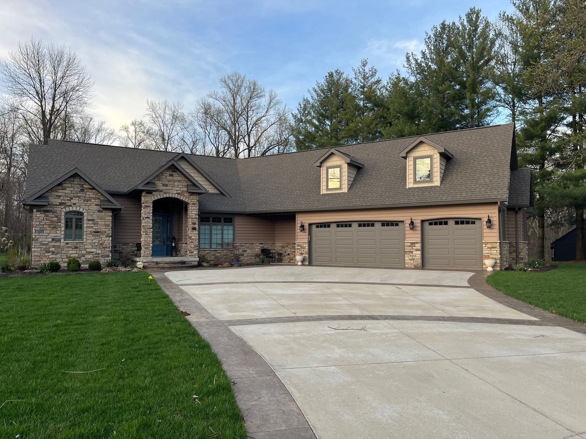 Gray-shingled roof with a chimney and dormer window, set against a backdrop of green trees.