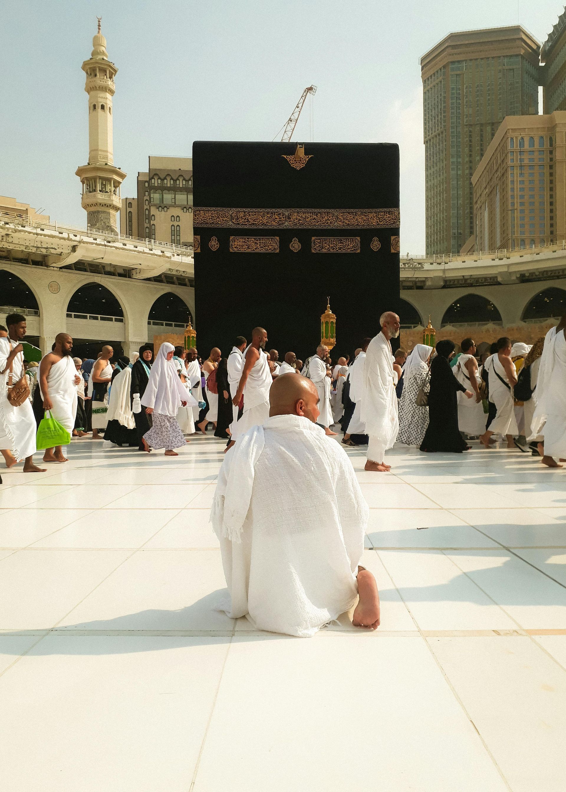 A man is kneeling in front of the kaaba in a mosque.