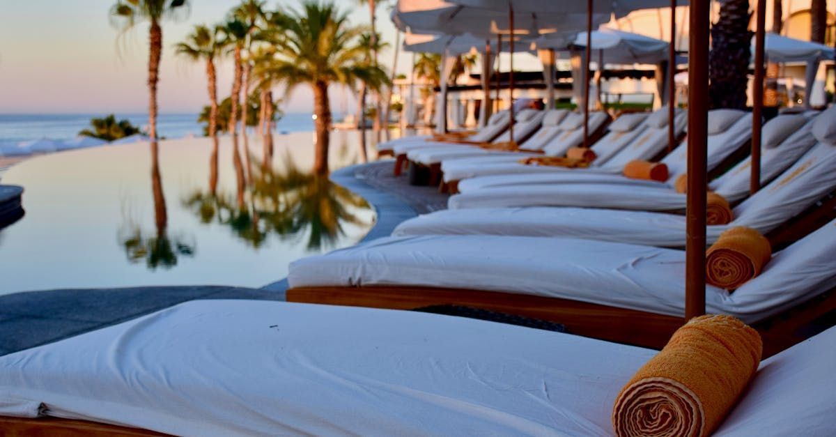 A row of lounge chairs next to a swimming pool with palm trees in the background.
