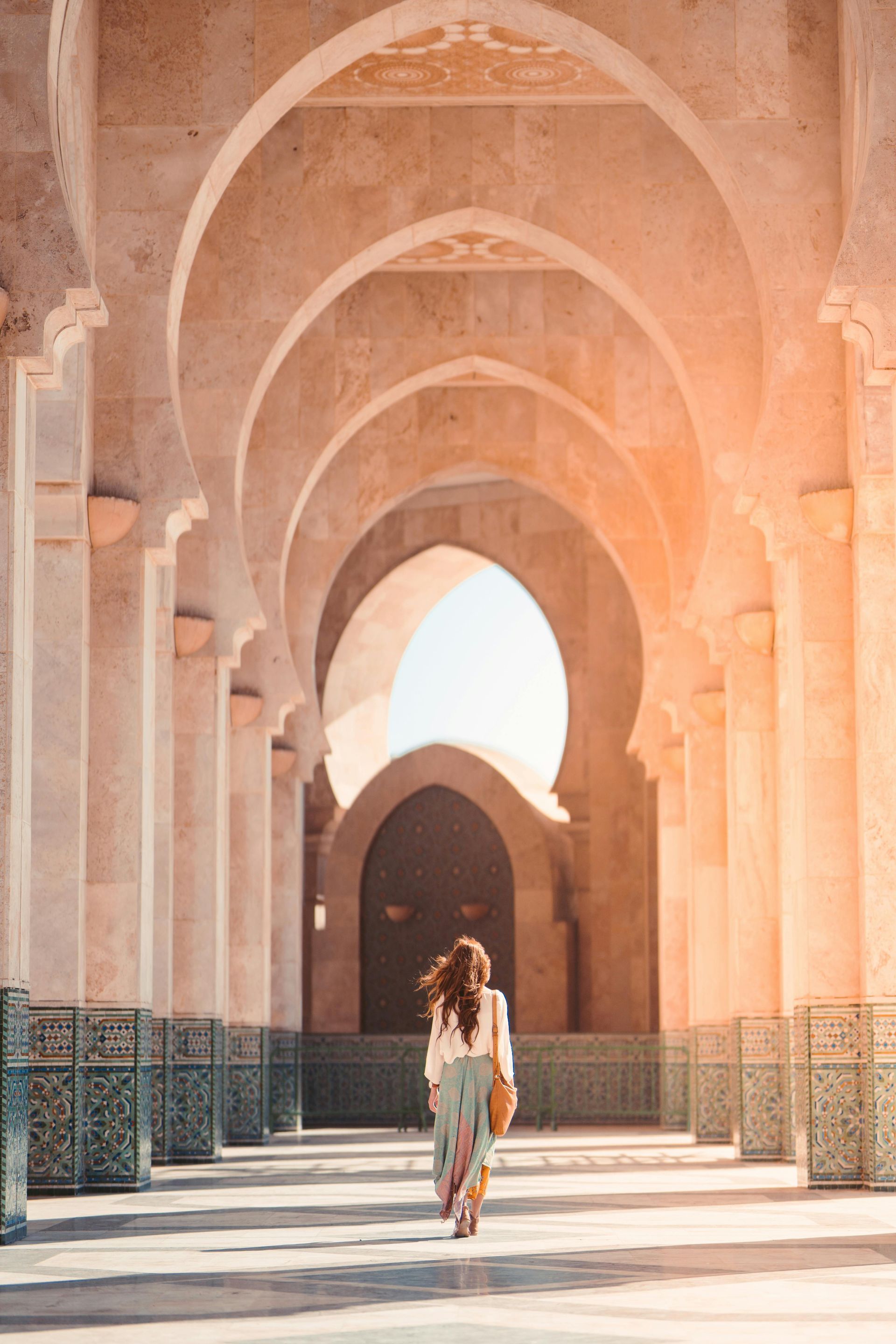 A woman is walking through a hallway of arches in a building.