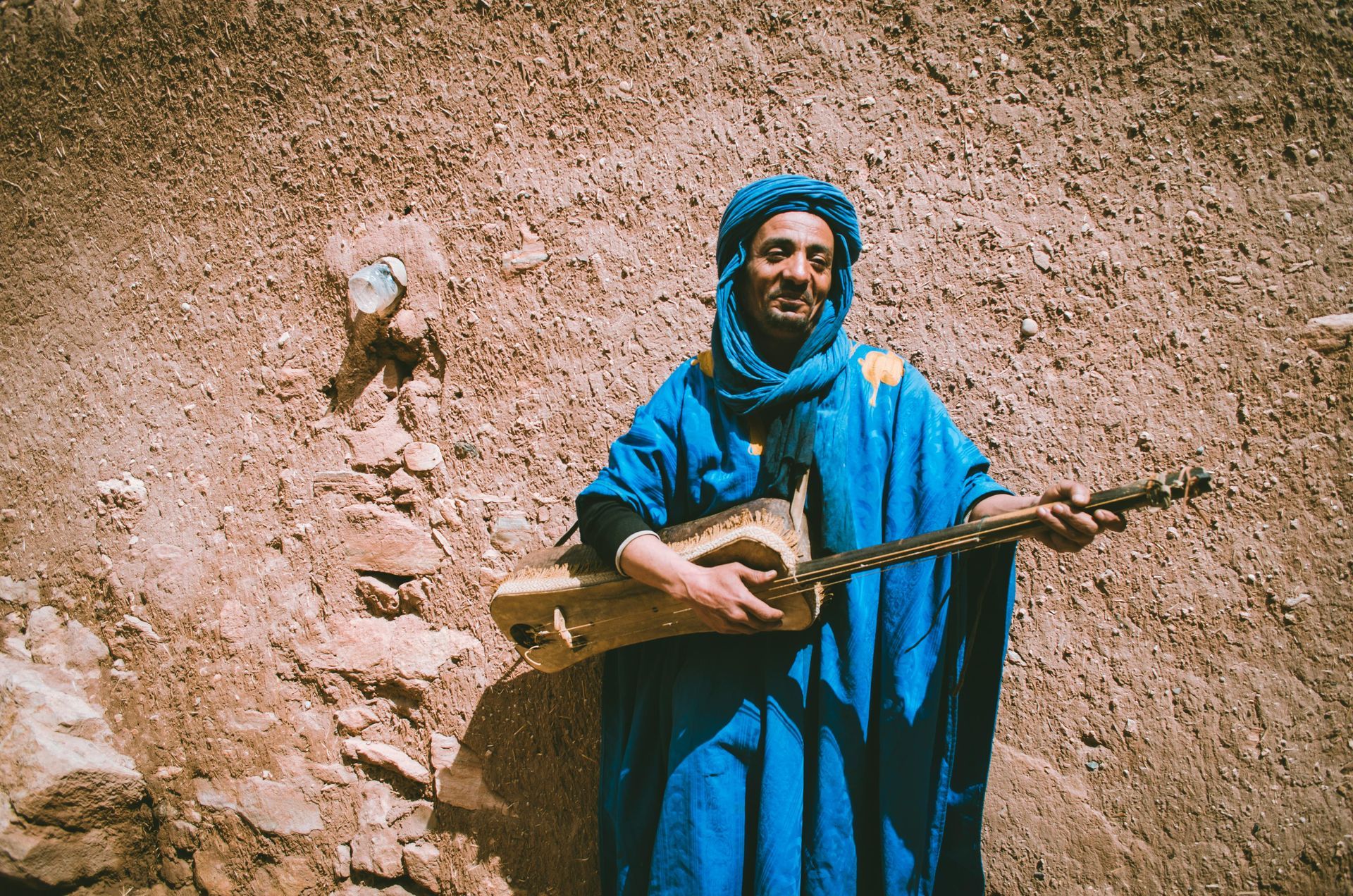 A man in a blue robe is playing a guitar in the desert