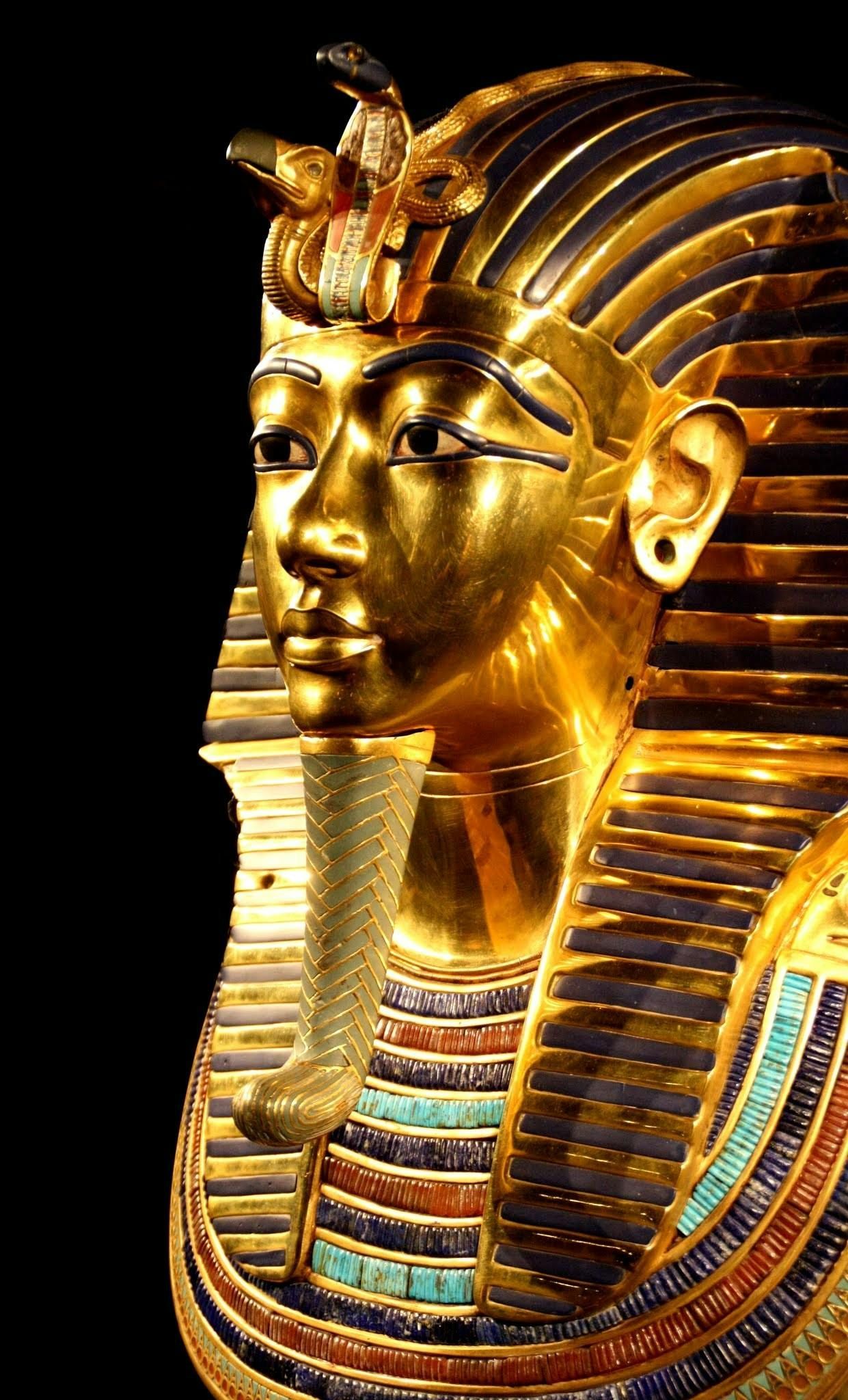 A close up of a gold mask of a pharaoh on a black background.