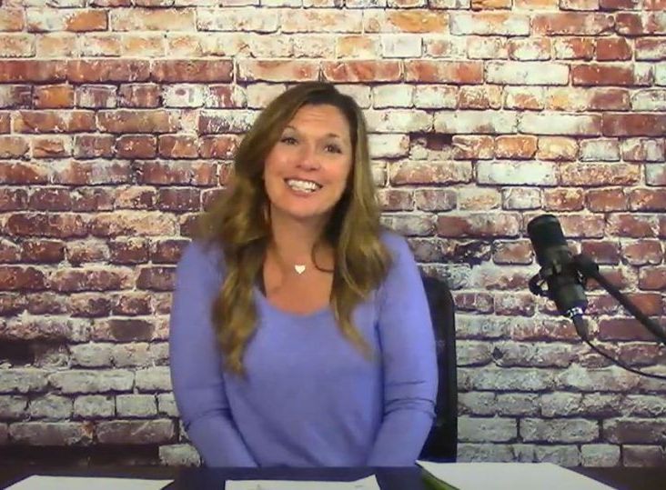 A woman in a purple sweater is sitting in front of a microphone in front of a brick wall.