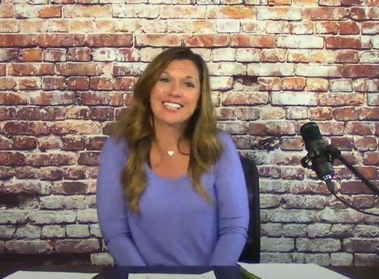 A woman in a purple sweater is sitting in front of a microphone in front of a brick wall.