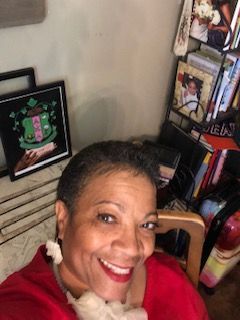 A woman is smiling while sitting in a chair in front of a bookshelf.