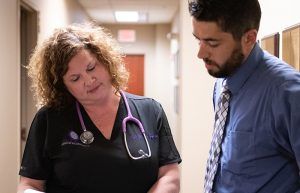 A man and a nurse are looking at a clipboard in a hallway.
