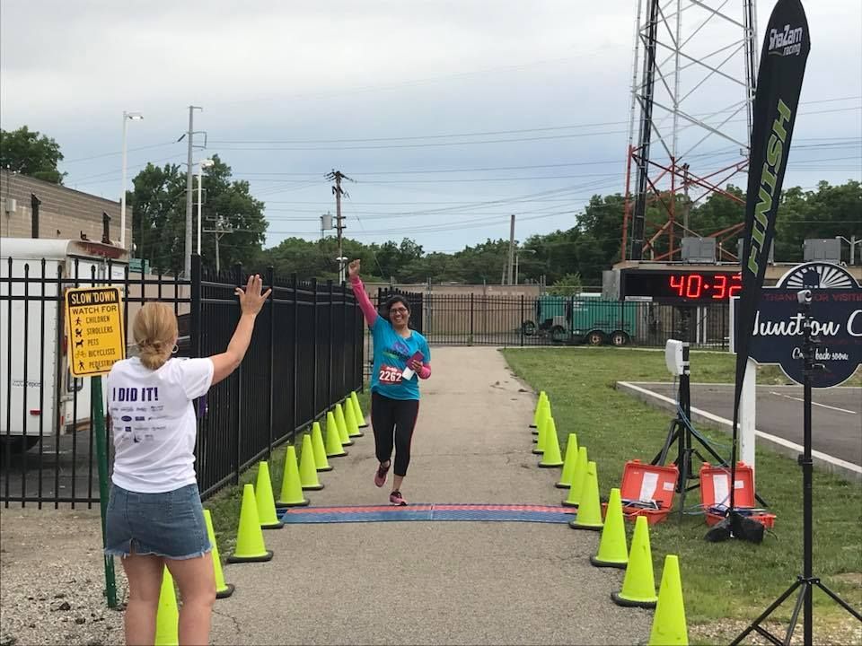 A woman in a white shirt is standing next to a woman running in a race.