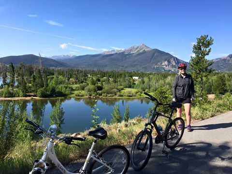 A woman is standing next to two bicycles next to a lake.