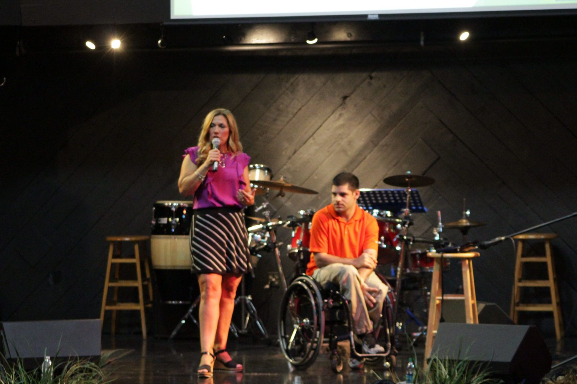A woman is standing next to a man in a wheelchair on a stage.