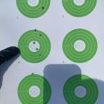 A person is pointing at a green target on a white surface.