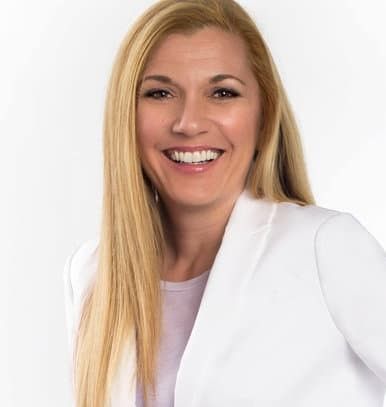 A woman with long blonde hair is wearing a white jacket and smiling.