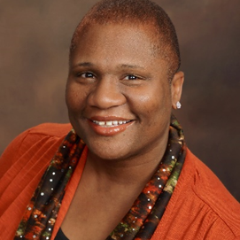 A woman wearing an orange sweater and a scarf smiles for the camera