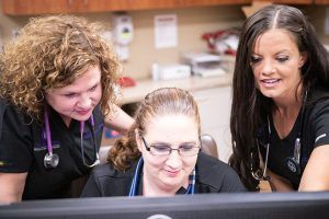 Three nurses are looking at a computer screen together.