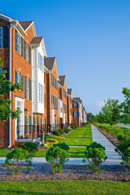 A row of brick apartment buildings with a sidewalk in front of them.