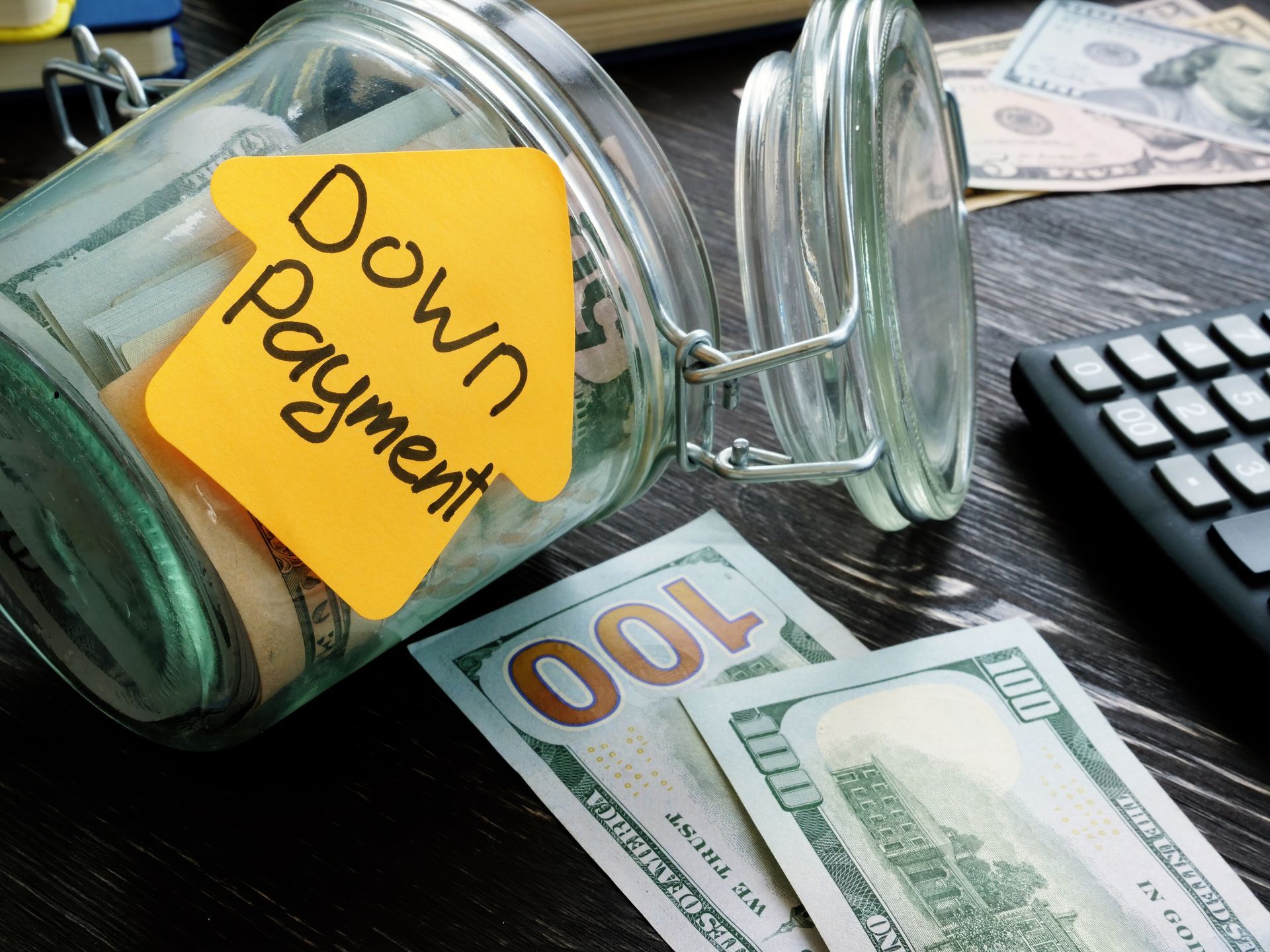 A glass jar filled with money and a yellow sticky note that says down payment.
