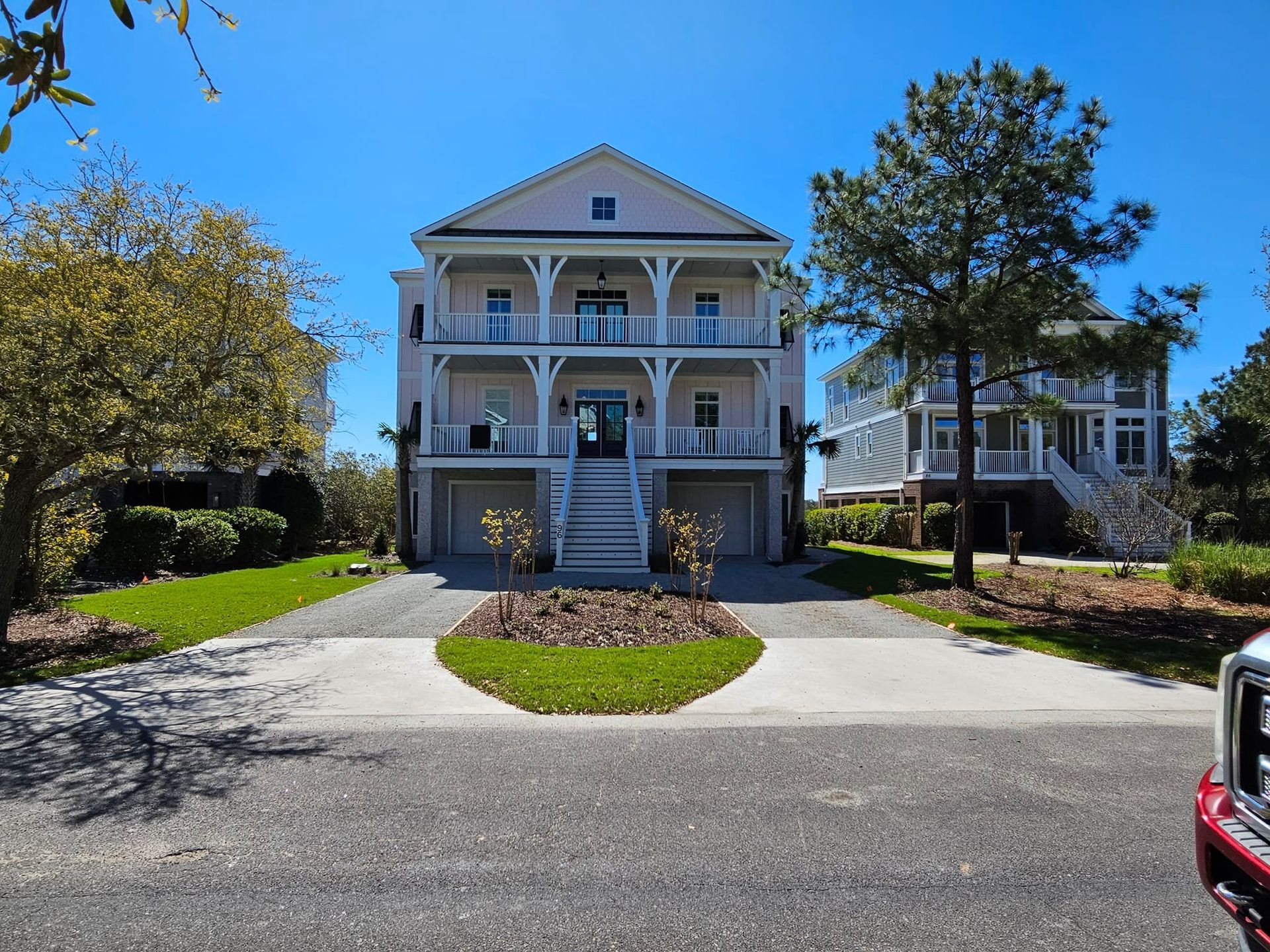Three-story light pink house with white trim, two levels of balconies, garages below, and a lush green lawn.
