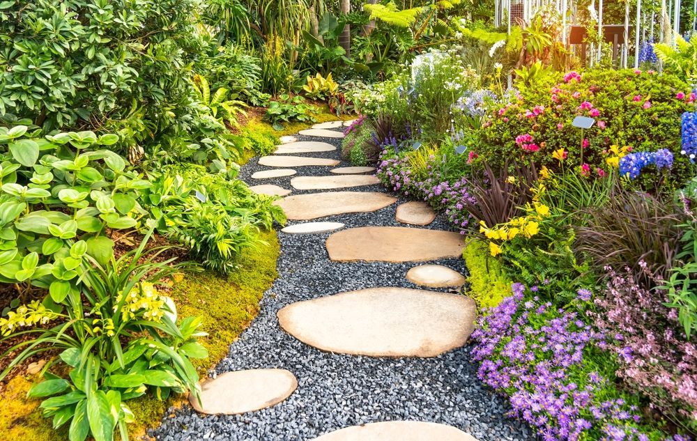 Stone path winds through lush garden with colorful flowers and greenery.